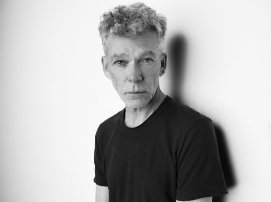 A black and white portrait of Paul Harvey wearing a dark t-shirt. / Une photo en noir et blanc de Paul Harvey portant un tee-shirt foncé.