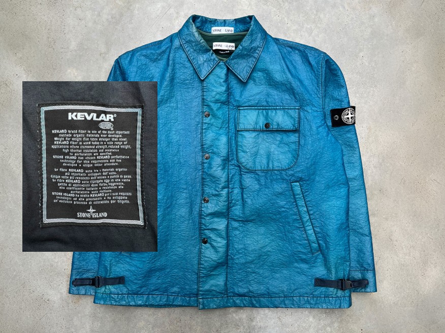An iridescent blue Kevlar jacket laid flat on a grey background. / Une veste en Kevlar bleue sur un arrière-plan gris.