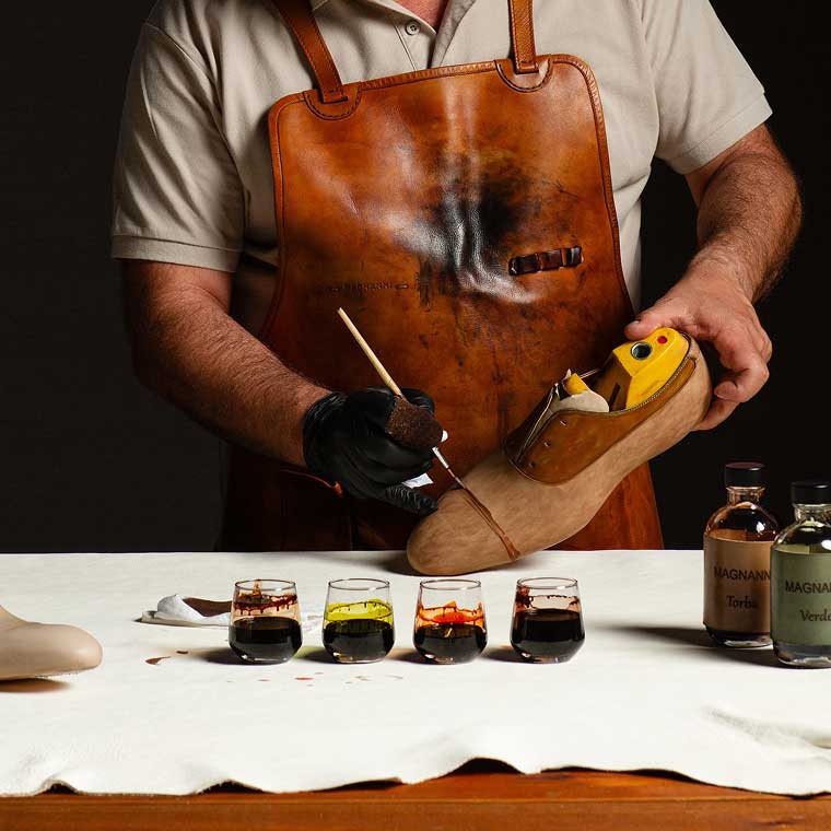A craftsman at his workbench hand-painting a leather dress shoe on a last.