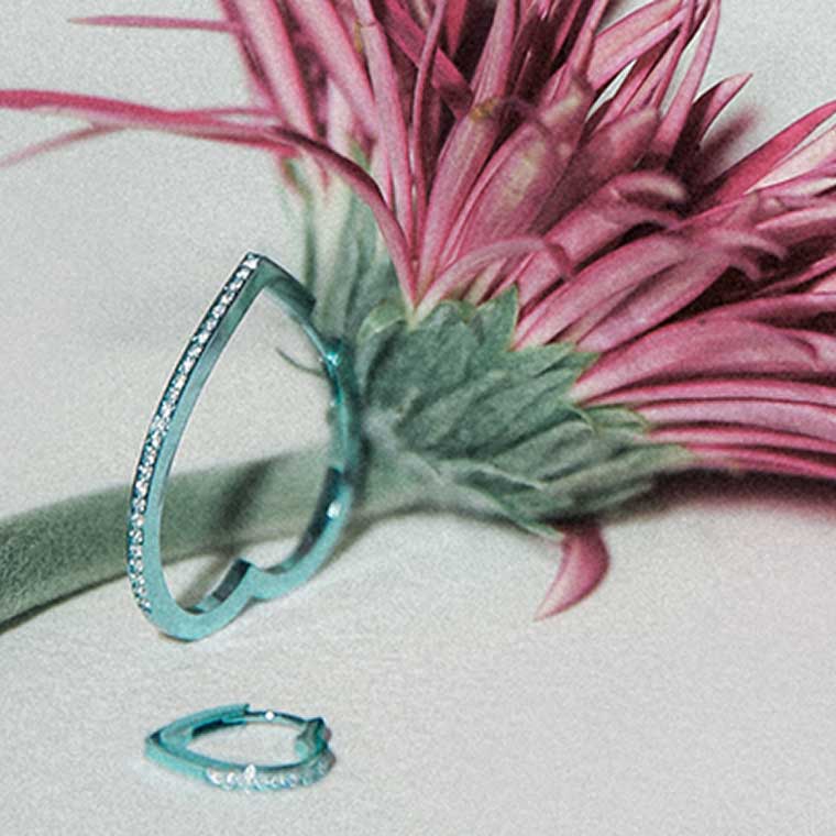 Two heart-shaped pieces of jewellery, styled next to a pink flower.