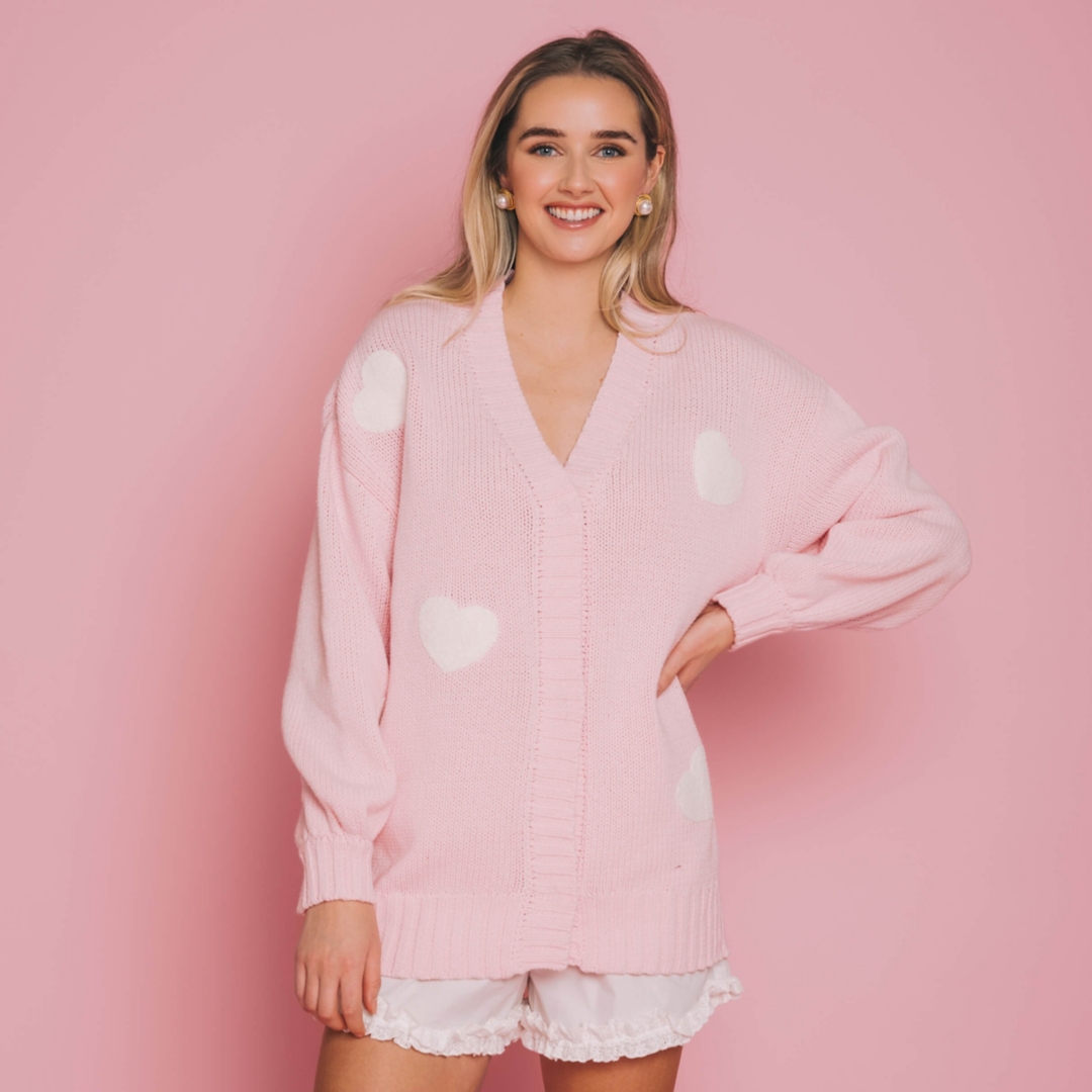 A model poses in a pink cardigan in front of a pink background